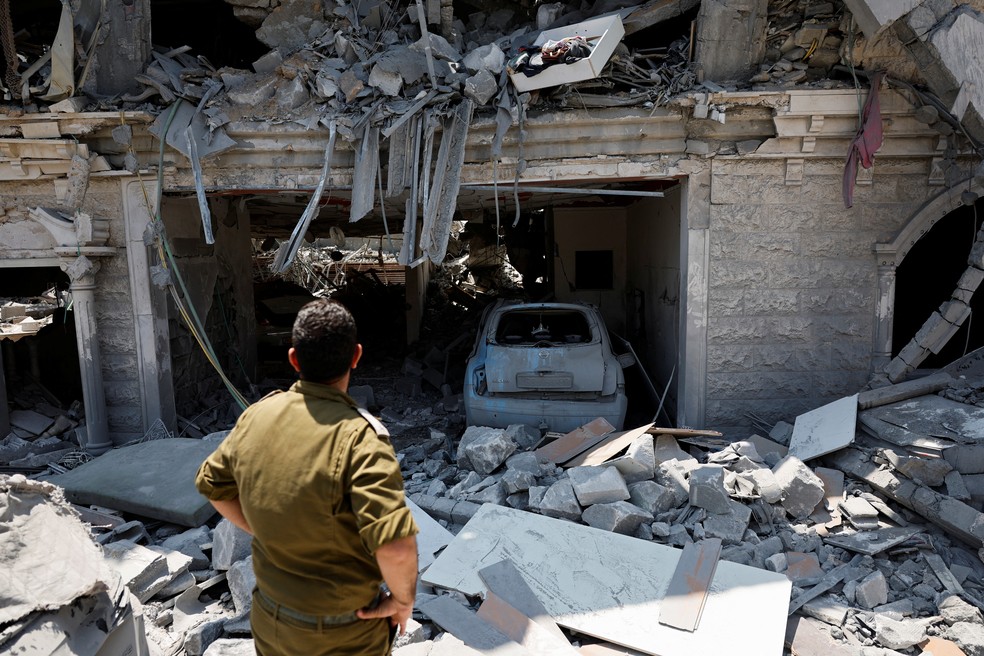 Um soldado israelense observa estragos após mísseis disparados do Irã atingirem um prédio residencial, em Tamra, norte de Israel, em 15 de junho de 2025 — Foto: Ammar Awad/Reuters