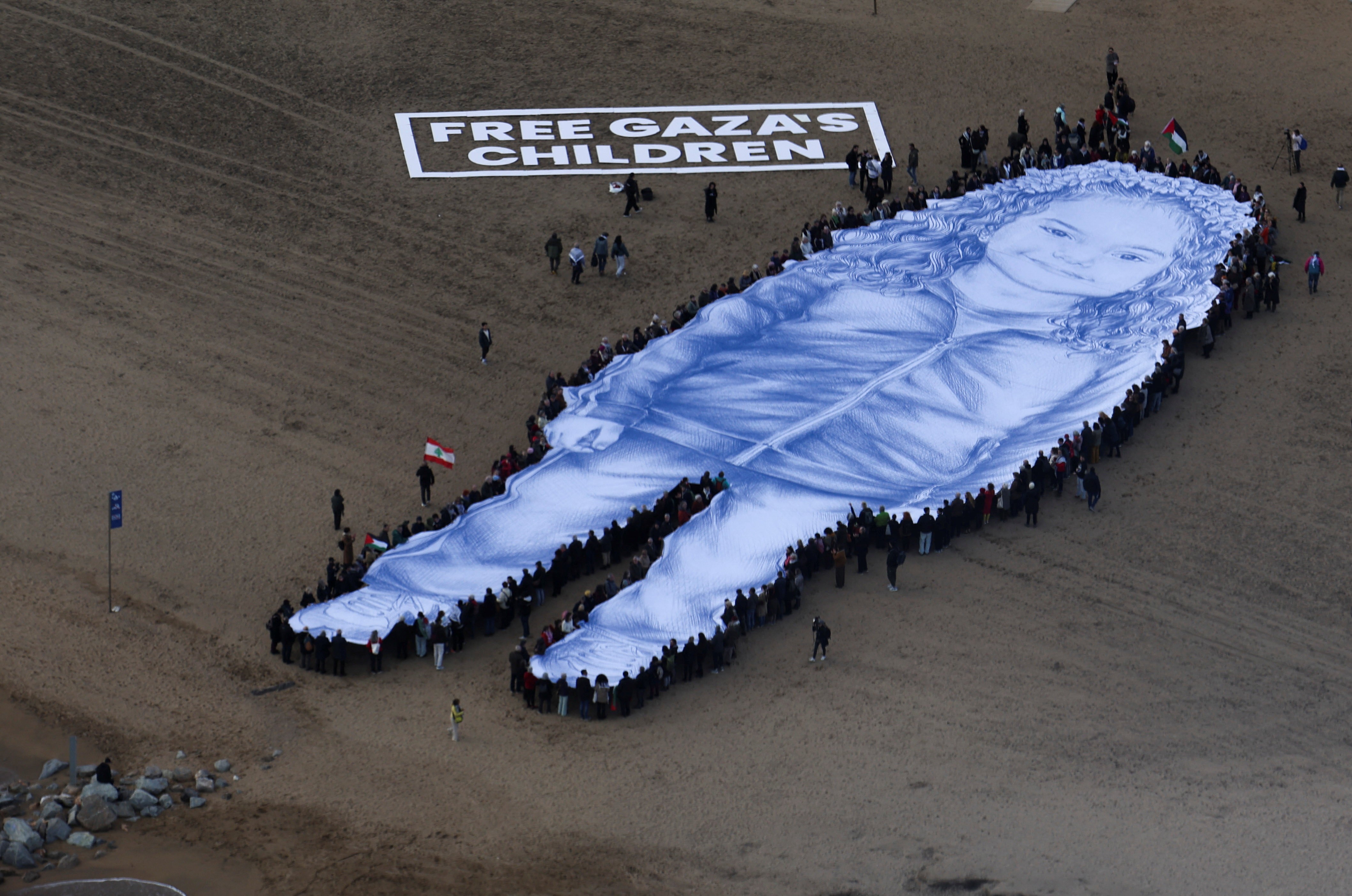 Retrato gigante de menina morta na guerra de Gaza é estendido em praia de Barcelona