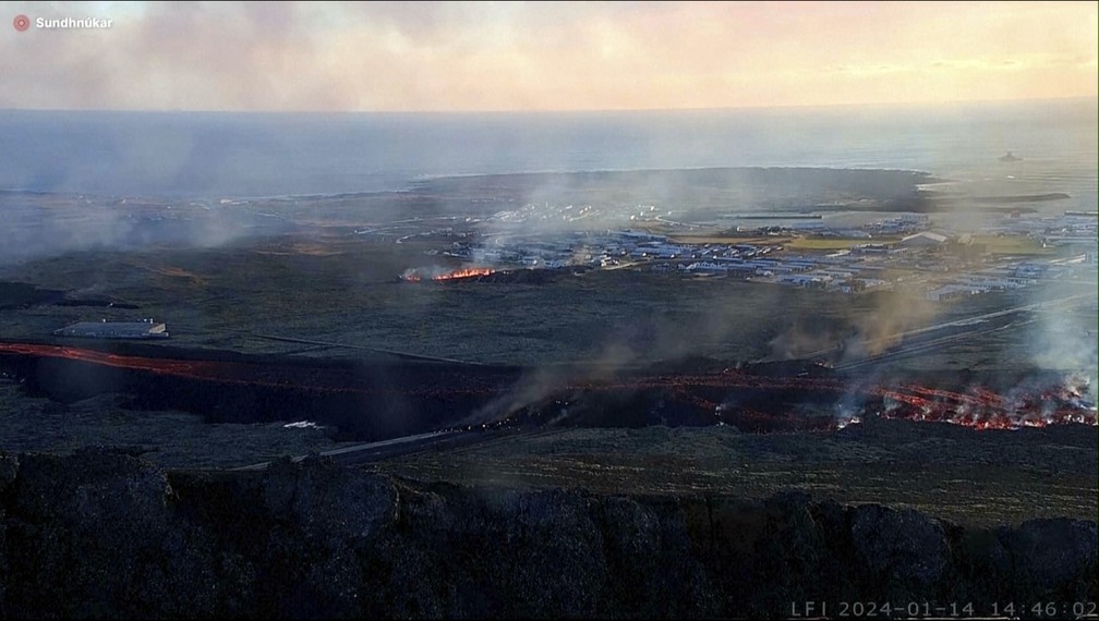Lava se move em direção a uma vila de pescadores na cidade de Grindavik, no sudeste da Islândia, e deixa residências em chamas após a erupção de um vulcão perto da região neste domingo, 14 de janeiro de 2024. A comunidade foi evacuada durante a noite. — Foto: LIVEFROMICELAND.IS via AP
