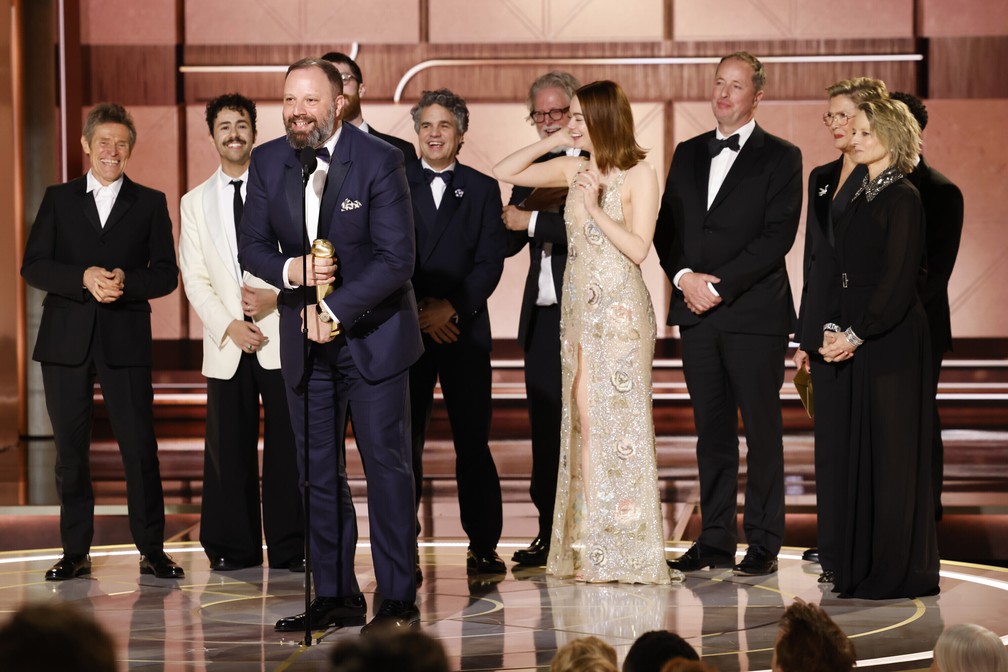 O diretor Yorgos Lanthimos recebe o prêmio de melhor filme de comédia ou musical para 'Pobres criaturas' com o elenco e as apresentadoras da categoria no Globo de Ouro 2024 — Foto: Sonja Flemming/CBS via AP