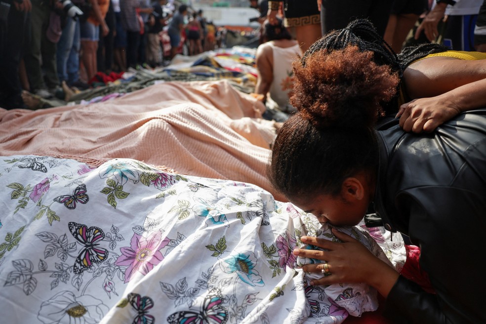 Mulher beija um dos corpos levados a praça no Complexo da Penha, na Zona Norte do Rio de Janeiro, no dia 29 de outubro de 2025 — Foto: Ricardo Moraes/Reuters