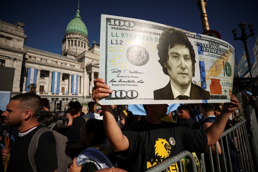 Um apoiador do novo presidente da Argentina segura uma nota de 100 dólares com uma imagem de Javier Milei durante a campanha — Foto: Agustin Marcarian / Reuters