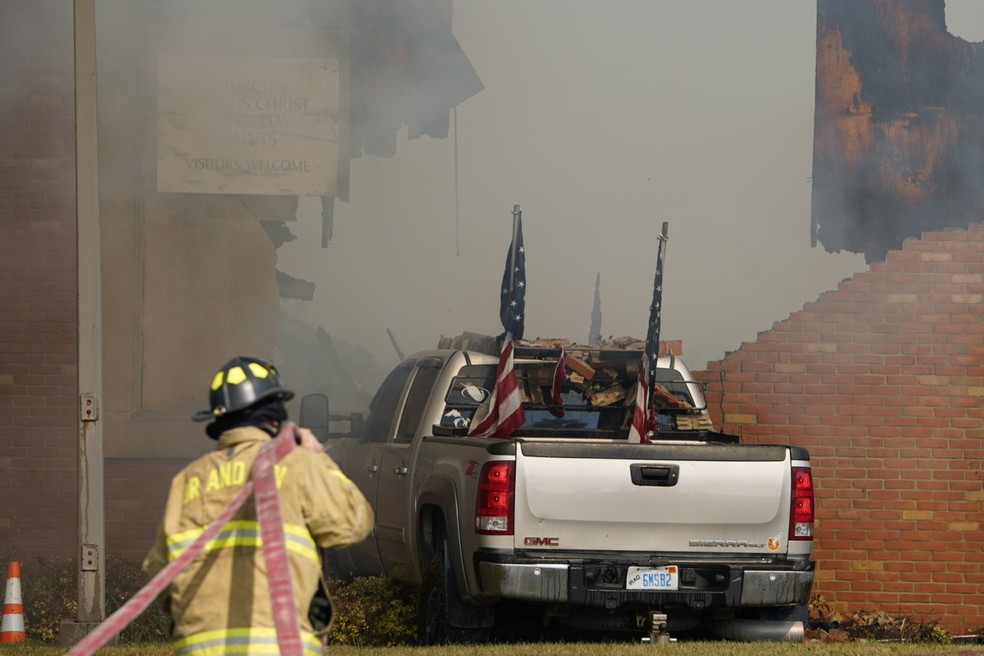 Veículo em chamas após colisão com o prédio enquanto bombeiro atua na igreja mórmon em Grand Blanc, Michigan. — Foto: Lukas Katilius/The Flint Journal via AP