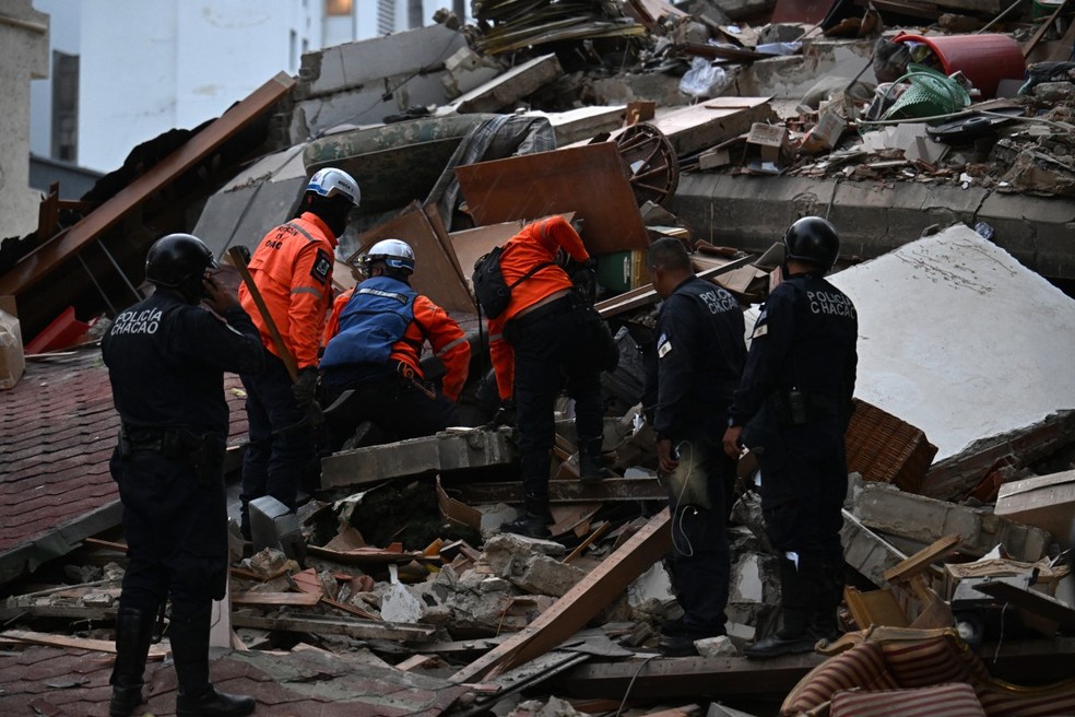 Equipes de resgate vasculham os escombros de uma estrutura que desabou, enquanto policiais municipais observam de perto, ap&oacute;s um terremoto em Caracas, em 24 de junho de 2026 &mdash; Foto: Juan Barreto/AFP
