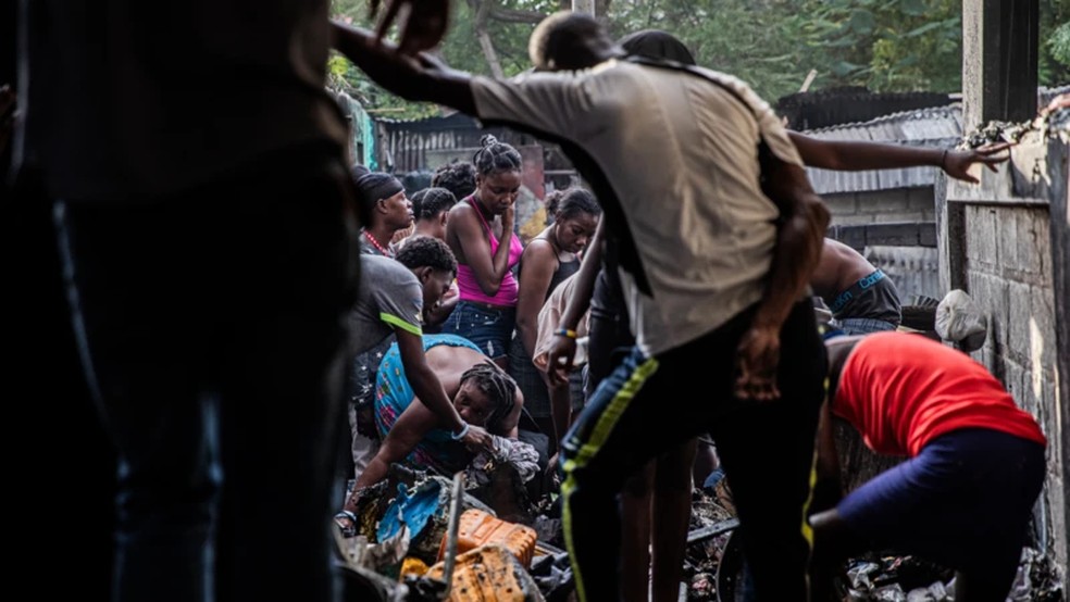 Pessoas fazem busca entre o que ficou para trás no incêndio em um campo de deslocados em Porto Príncipe, no Haiti, em 21 de dezembro de 2025 — Foto: Clarens Siffroy via BBC