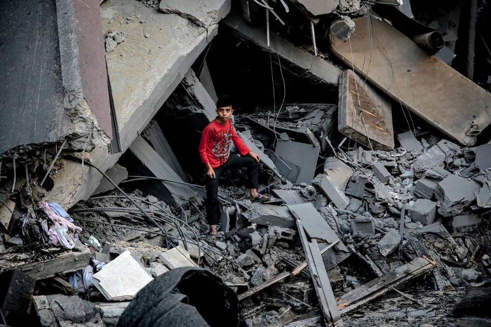 Menino palestino em frente a escombros de edifício após ataque israelense à Cidade de Gaza, em 26 de outubro de 2023 — Foto: Omar El-Qattaa / AFP
