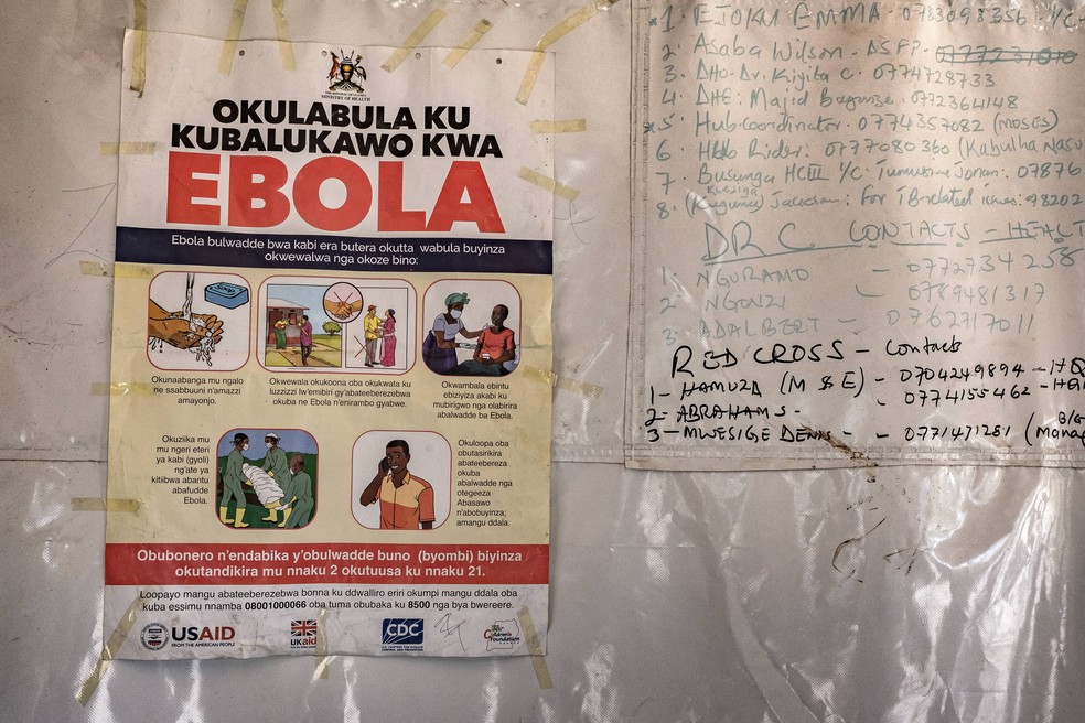 Cartaz com os números de contato de emergência para o Ebola está afixado em uma tenda na passagem de fronteira de Busunga, entre Uganda e a República Democrática do Congo, em Bundibugyo, em 18 de maio de 2026 — Foto: BADRU KATUMBA / AFP