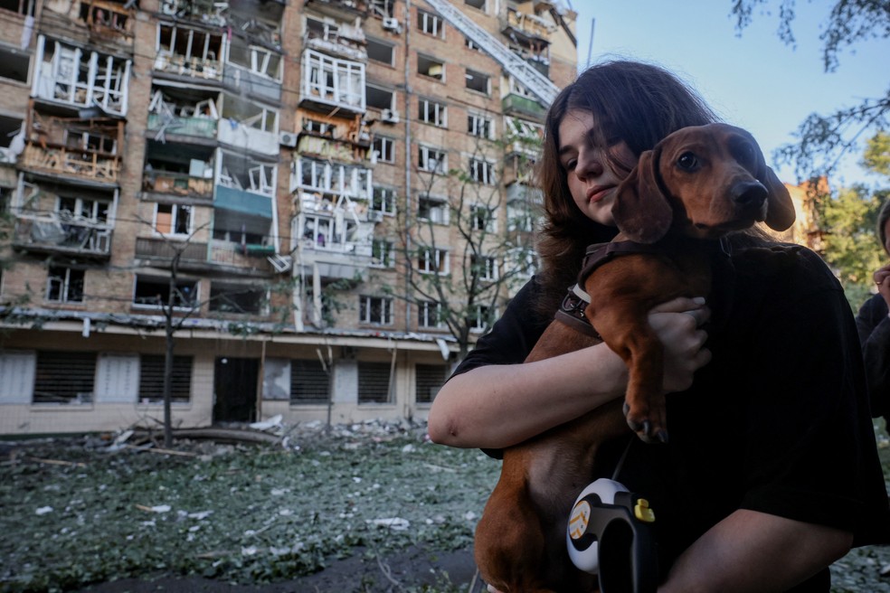 Moradora segura cachorro em frente a prédio destruído após ataque russo a Kiev no domingo (24) — Foto: REUTERS/Thomas Peter